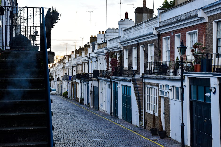 A row of multi-story residential buildings with distinctive bay windows and detailed architectural mouldings, painted in various shades of blue, beige, and green, situated on a city street during dayt